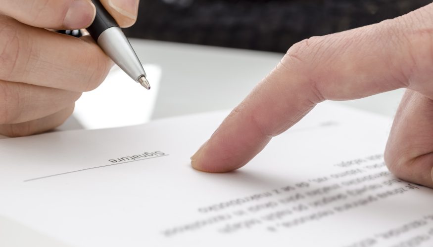 Detail of a woman signing a paper. Male finger showing where to sign.